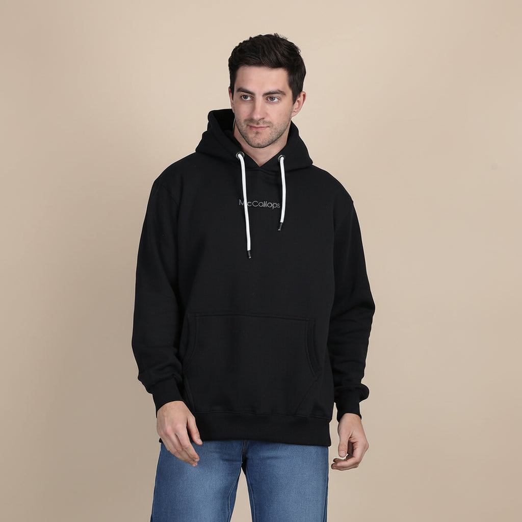 Model wearing a McCallops premium heavyweight black hoodie in a minimalist studio setting.